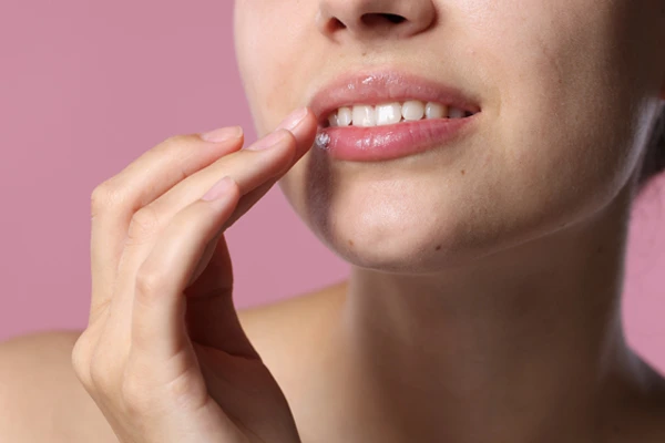 Kobieta o naturalnym wyglądzie dotyka okolic swoich ust. 